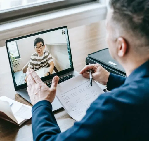 Person on a laptop video call while making notes on a printout